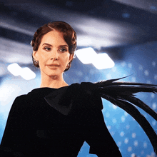 a woman in a black dress with feathers on her shoulder is looking at the camera