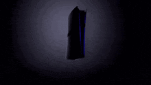 a black ps5 is floating in the air in the dark .