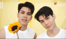 two young men standing next to each other holding a sunflower .