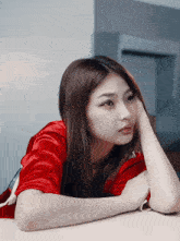 a woman in a red shirt leans on a table with her head resting on her hand