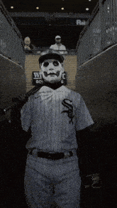 a baseball player with a mask on his face is holding a bat in a tunnel .