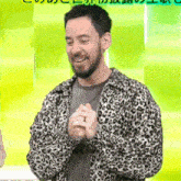 a man with a beard wearing a leopard print jacket is standing in front of a green background .