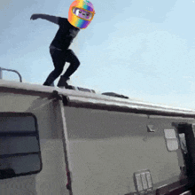 a person wearing a rainbow helmet is standing on the roof of a camper