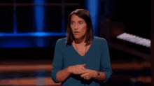 a woman in a blue shirt is standing on a stage with her hands together and making a funny face .