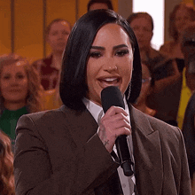 a woman in a brown suit and white shirt is smiling in front of a crowd .
