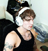 a man wearing headphones and a black tank top with a tattoo on his arm
