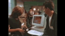 a man and a woman are standing in front of a computer monitor .