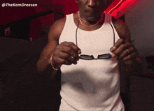 a man wearing a white tank top is holding a pair of sunglasses with the hashtag @thekamdreesen on the bottom right