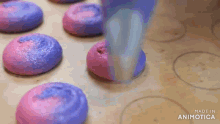 a person is making purple and pink macarons with sprinkles on them .