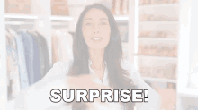 a woman in a white shirt says surprise in front of a wardrobe