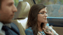 a woman wearing glasses sits in a car with a man