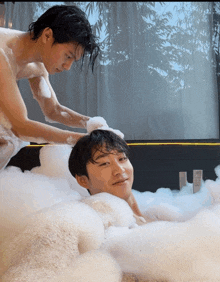 a man washing another man 's head in a bubble bath
