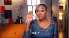 a woman in a blue dress is waving her hand and saying bye .