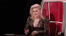 a woman in a sequined dress is sitting in a red chair on the voice
