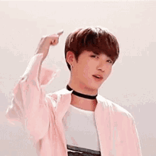 a young man wearing a choker and a pink jacket is pointing his finger at the camera .