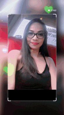 a woman wearing glasses and a black tank top has the number 3762 on her phone