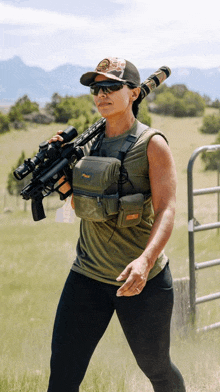 a woman is carrying a rifle in a field with mountains in the background ..