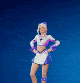 a cheerleader in a purple and white outfit is holding a pink heart in her hands
