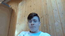 a young man sitting in front of a wooden wall looking at the camera