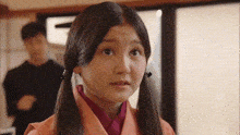 a girl with pigtails is looking at the camera with a man standing behind her .