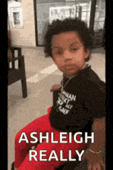 a young boy is sitting in a chair and making a funny face while wearing a black shirt and red pants .
