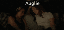 two women are laying on a couch and the word auglie is on the bottom