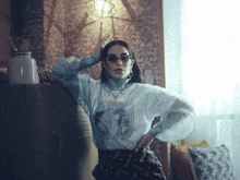 a woman wearing sunglasses and a turtleneck stands in a dark room