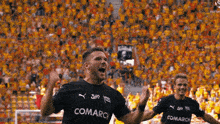 a soccer player wearing a black comarch jersey is celebrating a goal