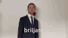 a man in a suit and tie stands in front of a white wall and says briljant