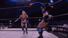two women are wrestling in a ring and one of them is wearing blue shorts .