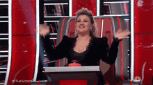 a woman is sitting in a chair with her arms outstretched in front of a sign that says " the voice "