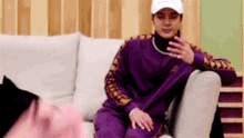 a man in a purple jacket is sitting on a couch with a white hat on .