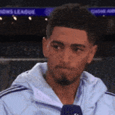 a man in a white jacket is talking into a microphone in front of a sign that says sports league