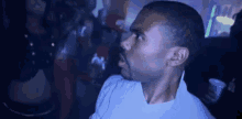a man in a white shirt is standing in a dark room with a crowd behind him .