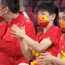 a group of people wearing red shirts and masks are clapping their hands .
