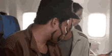 a man with a beard is sitting on an airplane looking at a cell phone .