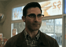 a man wearing glasses and a plaid shirt stands in front of a sign that says ' ice cream ' on it