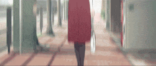 a woman in a red skirt and black tights is walking down a hallway