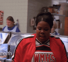 a woman wearing a red wmhs jacket stands in a kitchen