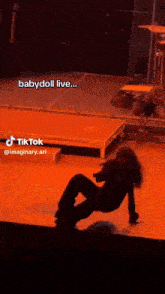 a woman is sitting on the edge of a stage at a concert and talking on a cell phone .
