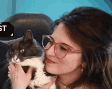 a woman wearing glasses holds a cat in front of a sign that says " st "