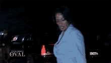 a woman in a white dress is standing in front of a car that says tyler perry 's the oval on the bottom