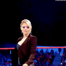 a woman is standing in a wrestling ring with a crowd behind her .