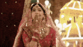 a bride in a red dress and veil is blowing a kiss with her hands .