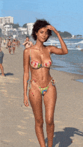 a woman in a bikini stands on the beach with her hands in her hair