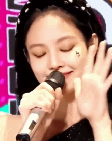 a woman is singing into a microphone with her eyes closed and a tattoo on her face .