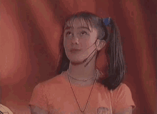 a young girl wearing a microphone and a necklace looks up .