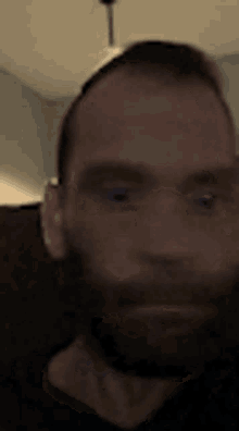 a man with a beard is sitting on a couch in a dark room .