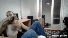 a shirtless man with a beard is sitting in a chair drinking a cup of coffee .