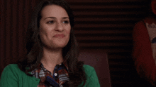 a woman wearing a green cardigan and plaid shirt makes a face
